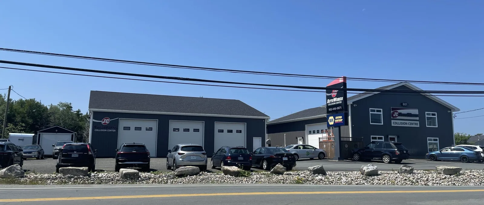 The JC AutoWorks collision centre at 801 Old Sambro Road in Harrietsfield, Nova Scotia — three bay doors, the NAPA-certified sign, and a full customer lot